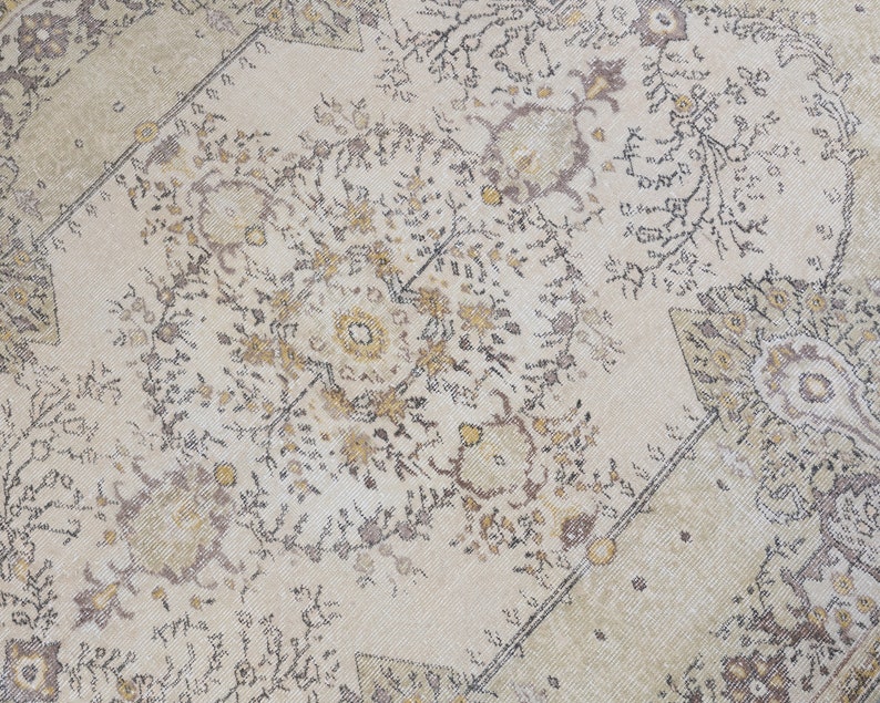 May include: Cream-colored area rug with an intricate floral pattern in shades of brown, gold, and black. The rug features a central medallion design and a border with geometric shapes. The rug's design is symmetrical and detailed.