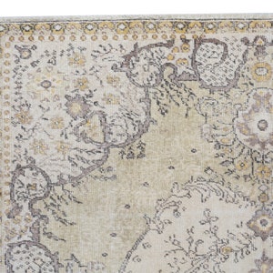 May include: Close-up of a section of a vintage-style rug. The rug features a cream-colored background with intricate floral and geometric patterns in shades of brown, gold, and gray. The edges have a decorative border.