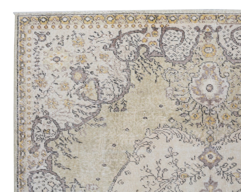May include: Close-up of a section of a vintage-style rug. The rug features a cream-colored background with intricate floral and geometric patterns in shades of brown, gold, and gray. The edges have a decorative border.