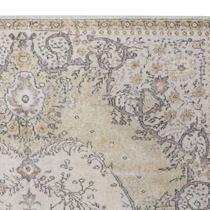 May include: Close-up of a section of a vintage-style area rug. The rug features a cream-colored background with intricate floral and geometric patterns in shades of brown, yellow, and gray. The edges have a decorative border.