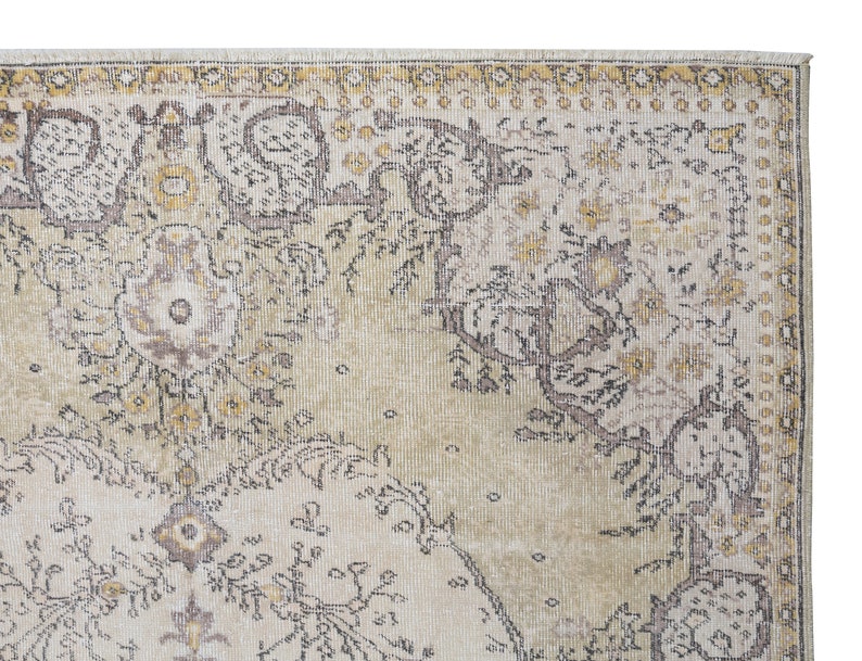 May include: Close-up of a section of a vintage-style area rug. The rug features a cream-colored background with intricate floral and geometric patterns in shades of brown, yellow, and gray. The edges have a decorative border.