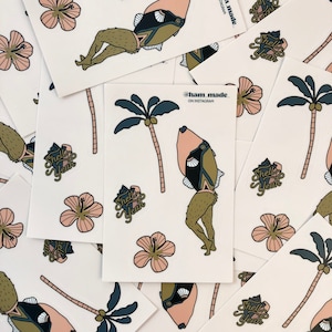 May include: A set of stickers featuring a cartoon fish wearing a bikini, a palm tree, and the phrase "Shell Yeah" in a yellow and brown font. The stickers are on a white background.
