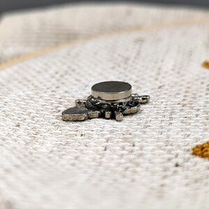 Back view of the bee needle minder attached to fabric, displaying its small, round magnetic piece.