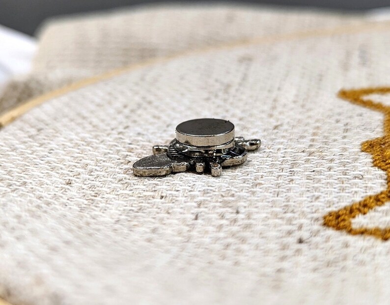 Back view of the bee needle minder attached to fabric, displaying its small, round magnetic piece.