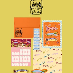 May include: A stationery set featuring a yellow background with a June calendar header, an orange envelope with a Snail Mail stamp, a July calendar page with fish illustrations, and various fish-themed cards and stickers in orange, pink, and blue.