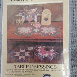 May include: A pattern for making table runners and mats in three sizes. The pattern features a patchwork design with pink, green, and white fabric. The pattern is titled "Classic Table Runners" and "Table Dressings". The pattern is by Donna Gallagher, Creative Needlearts, Inc.