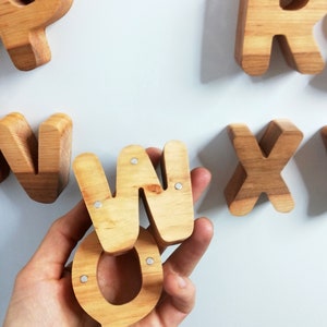 May include: Wooden letters in the shape of the letters W, Q, and R. The letters are made of light brown wood and have a natural finish. The letters are arranged in a random order.