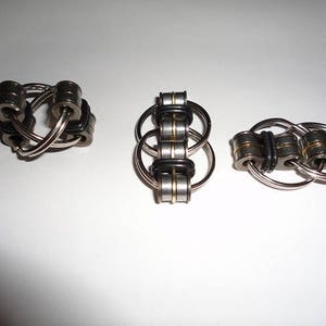 May include: Three silver and black metal fidget toys with interlocking rings. The toys are made of metal and have a polished finish.