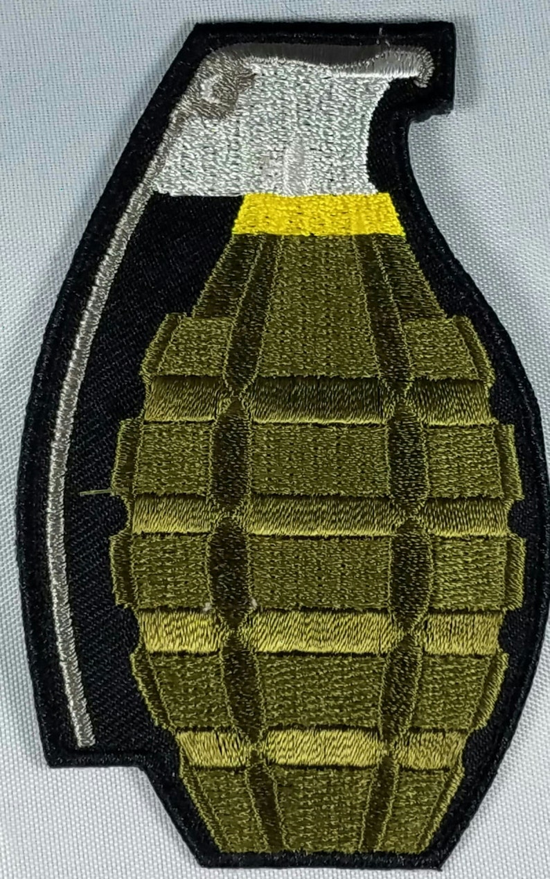 May include: A green and black embroidered patch of a grenade with a yellow pull pin.