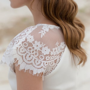 May include: A white wedding dress with a lace overlay on the shoulders. The dress has a simple, elegant design.