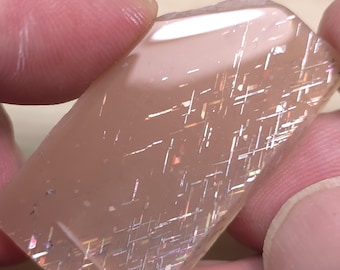 May include: A translucent pink gemstone with iridescent lines and a rough, natural shape.