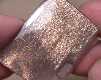 May include: A large, iridescent, rectangular sunstone crystal with a light brown color and a shimmery, metallic sheen.