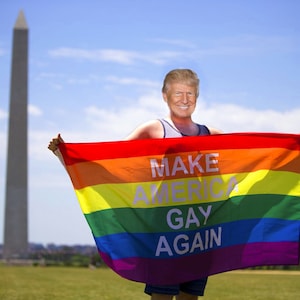 May include: A person holding a rainbow pride flag with the text "Make America Gay Again" printed on it. The flag is held in front of the Washington Monument.
