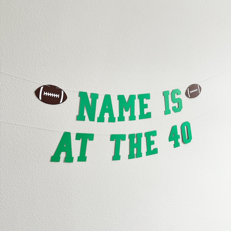 Puede incluir: Pancarta de papel verde y marr&oacute;n con el texto "NAME IS AT THE 40" y dos balones de f&uacute;tbol marrones.