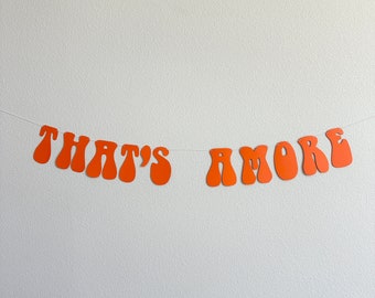 May include: Orange paper banner with the text "That's Amore" in a retro font style.