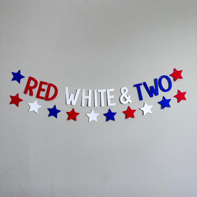 May include: Red, white, and blue star-shaped paper cutouts with the words "Red White & Two" strung together on a white wall.