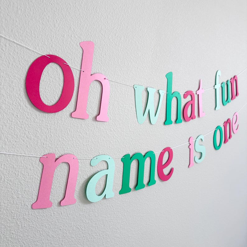 Puede incluir: Una pancarta de papel rosa, verde y roja con el texto "Oh what fun name is one".