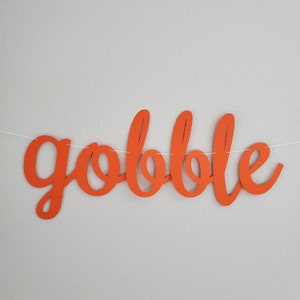 May include: Orange paper banner with the word "gobble" written in a cursive font.