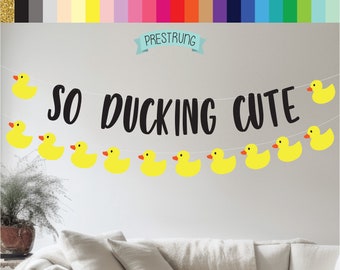 May include: A yellow rubber ducky banner with the text "SO DUCKING CUTE" in black. The banner is strung with white string and has yellow rubber ducky cutouts.