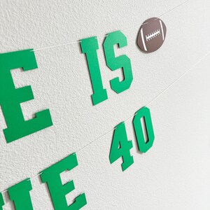 Puede incluir: Pancarta verde y blanca con el texto "He is 40" y una pelota de f&uacute;tbol marr&oacute;n.