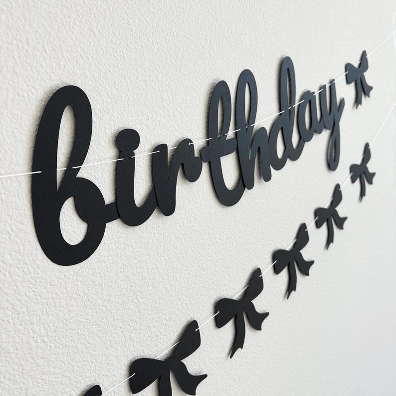 Pode incluir: Faixa de anivers&aacute;rio preta e branca com a palavra "anivers&aacute;rio" em letras grandes e cursivas e uma sequ&ecirc;ncia de la&ccedil;os pretos.