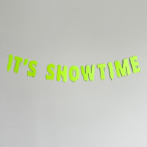 May include: A green paper banner with the words "IT'S SHOWTIME" in dripping letters.