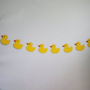 May include: A yellow rubber ducky garland with seven ducks strung together with white string. The ducks are all facing the same direction and have orange beaks.
