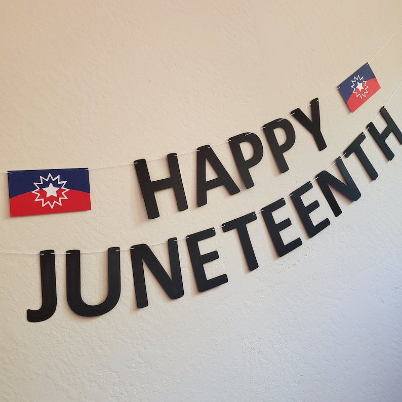 May include: A black banner with the words "Happy Juneteenth" in large, bold letters. Two small flags with a red, white, and blue star design are hanging from the banner.