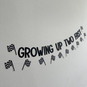 Puede incluir: Banderas a cuadros en blanco y negro y las palabras "Growing Up Two Fast" en una pared blanca. Esta es una pancarta para una fiesta de cumplea&ntilde;os.
