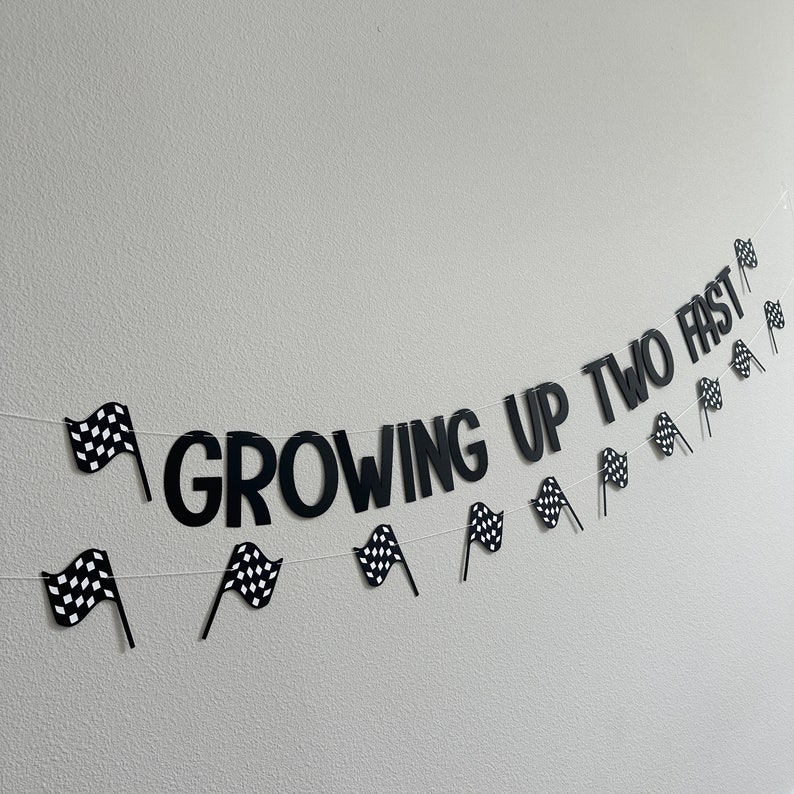 Puede incluir: Banderas a cuadros en blanco y negro y las palabras "Growing Up Two Fast" en una pared blanca. Esta es una pancarta para una fiesta de cumplea&ntilde;os.