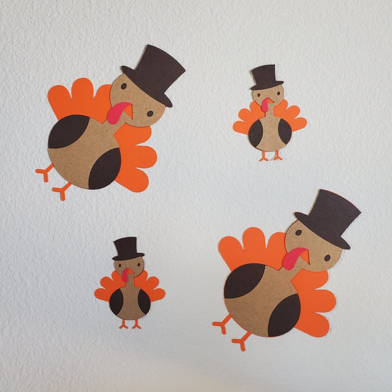 May include: Four paper turkeys with orange and brown feathers and black top hats. The turkeys are cut out and arranged on a white background.