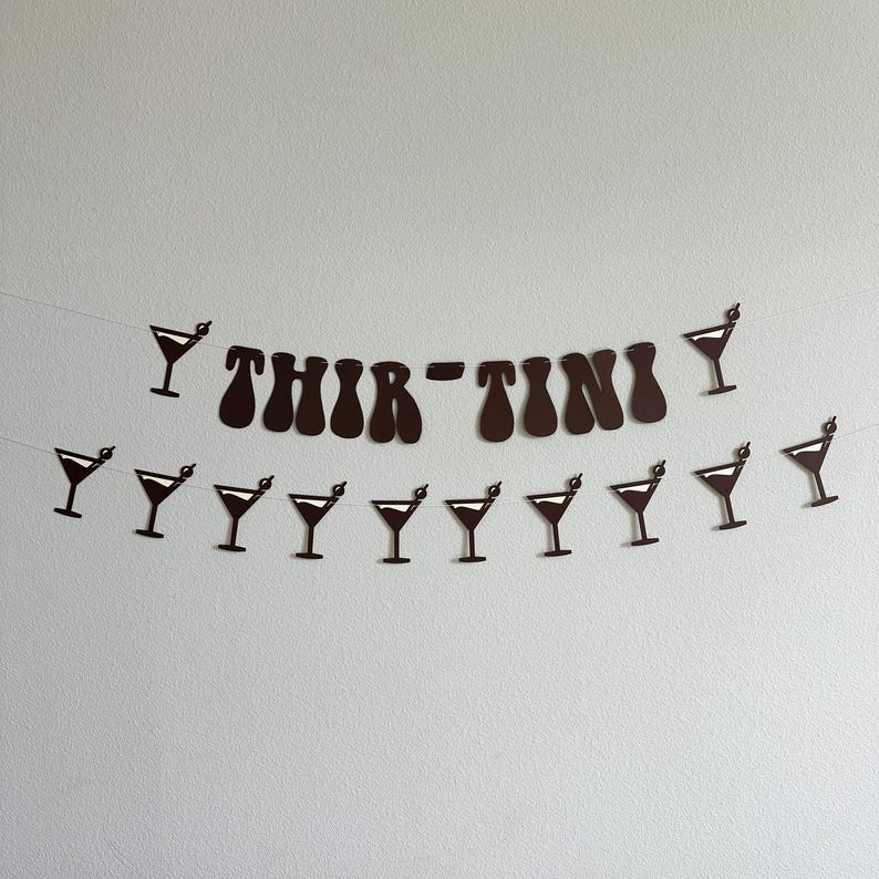 May include: Black and white paper banner with the text "Thir-tini" and a series of martini glasses. The banner is strung together with white string.