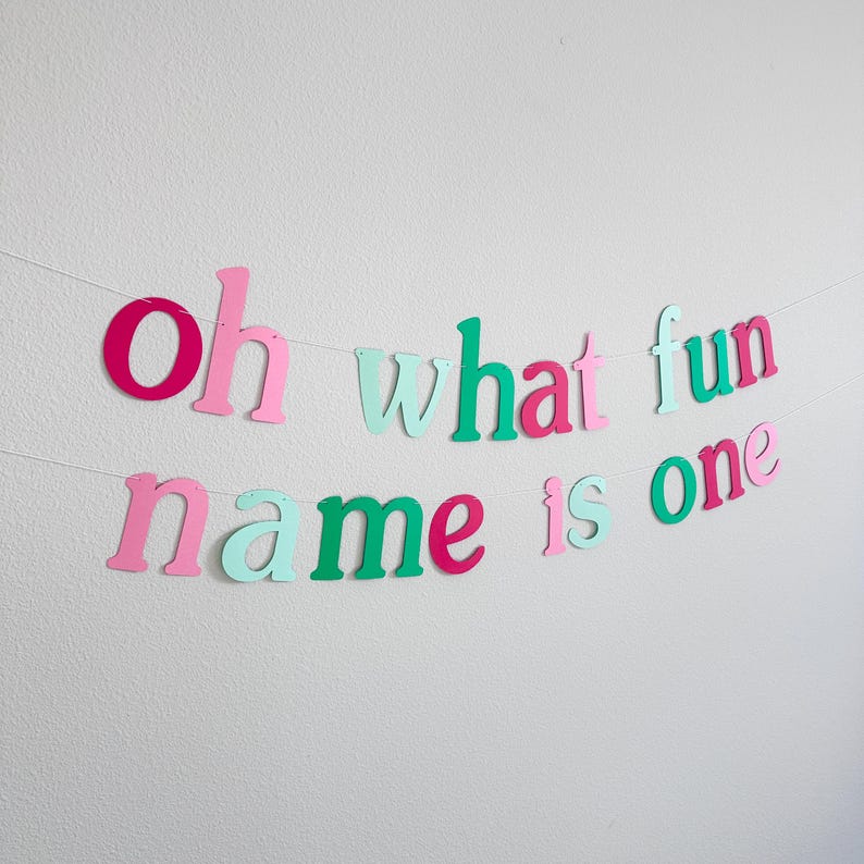 Puede incluir: Una pancarta de papel colorida con la frase "Oh what fun name is one" en letras rosas, verdes y blancas. La pancarta es perfecta para una fiesta de primer cumplea&ntilde;os.