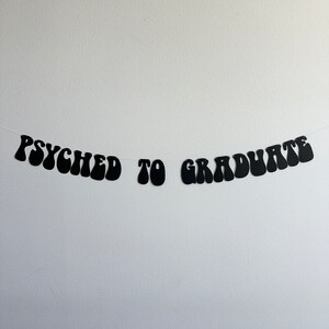 May include: Black and white banner with the text "Psyched to Graduate" in a retro font.