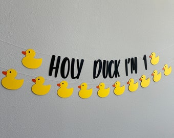 May include: A yellow rubber ducky banner with the text "HOLY DUCK I'M 1" in black. The banner is strung with yellow rubber ducky cutouts.