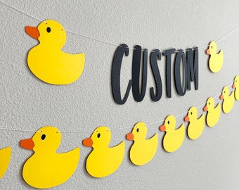 May include: A yellow rubber ducky banner with the word "CUSTOM" in black letters. The banner is strung with white string and includes several yellow rubber ducky cutouts.