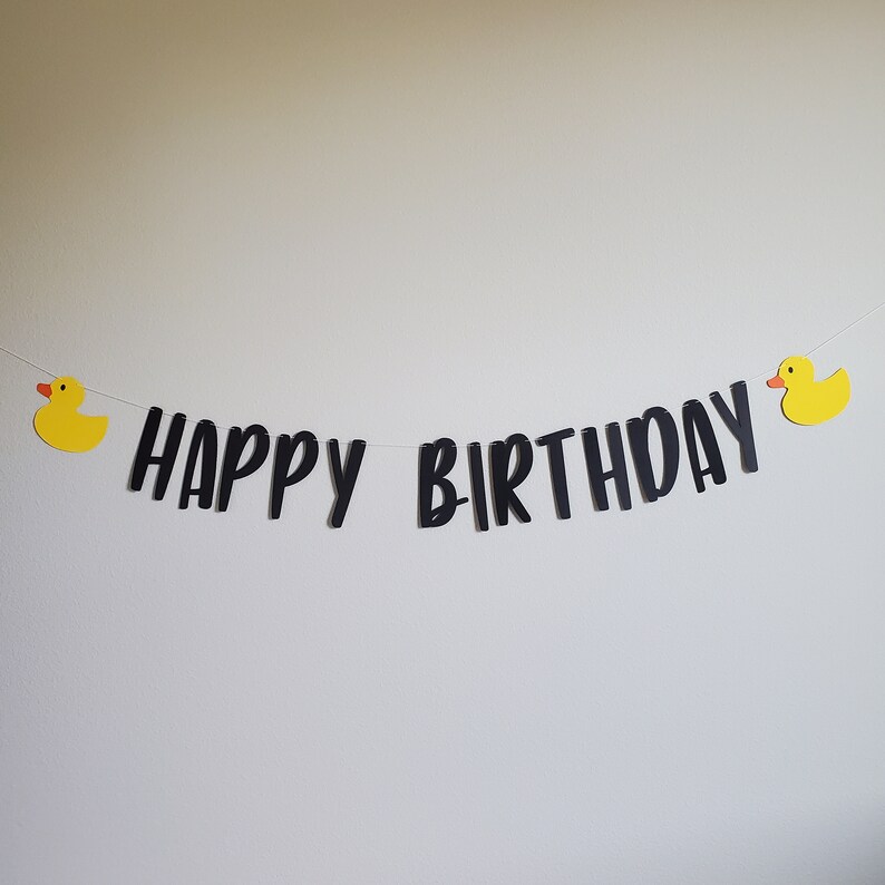 May include: Black and white "Happy Birthday" banner with yellow rubber duck decorations on each end.