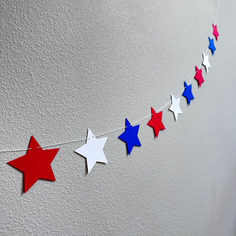 May include: A string of red, white, and blue paper stars hanging on a wall. The stars are connected by a white string.