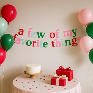 May include: A festive scene with red, green, and pink balloons, a cake on a wooden stand, and red gift boxes with bows. A banner reads "a few of my favorite things" in colorful letters. The table is covered with a pink cloth with confetti.