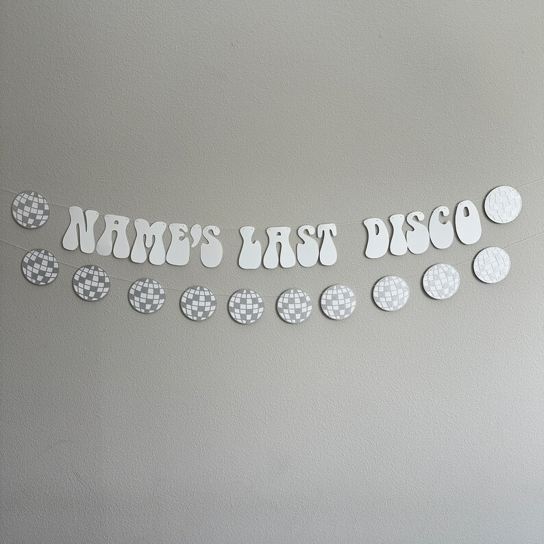 Pu&ograve; includere: Striscione bianco con il testo "NAME'S LAST DISCO" in un font retr&ograve;. Lo striscione &egrave; decorato con ritagli di sfere disco argentate con glitter.