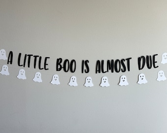 Könnte beinhalten: Ein weißes Geisterbanner mit schwarzem Text, der "A little boo is almost due" lautet. Das Banner ist mit weißen Geister-Ausschnitten bespannt.