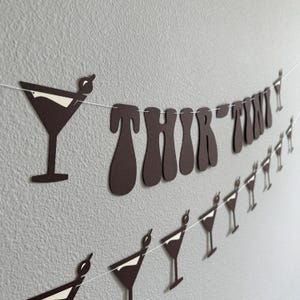 May include: Brown paper banner with the words "THIRTY TWO" in a retro font. The banner is decorated with white paper cutouts of martini glasses.