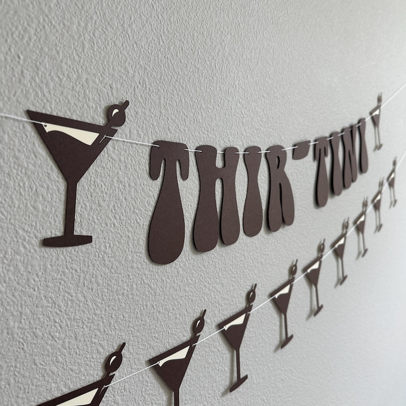 May include: Brown paper banner with the words "THIRTY TWO" in a retro font. The banner is decorated with white paper cutouts of martini glasses.