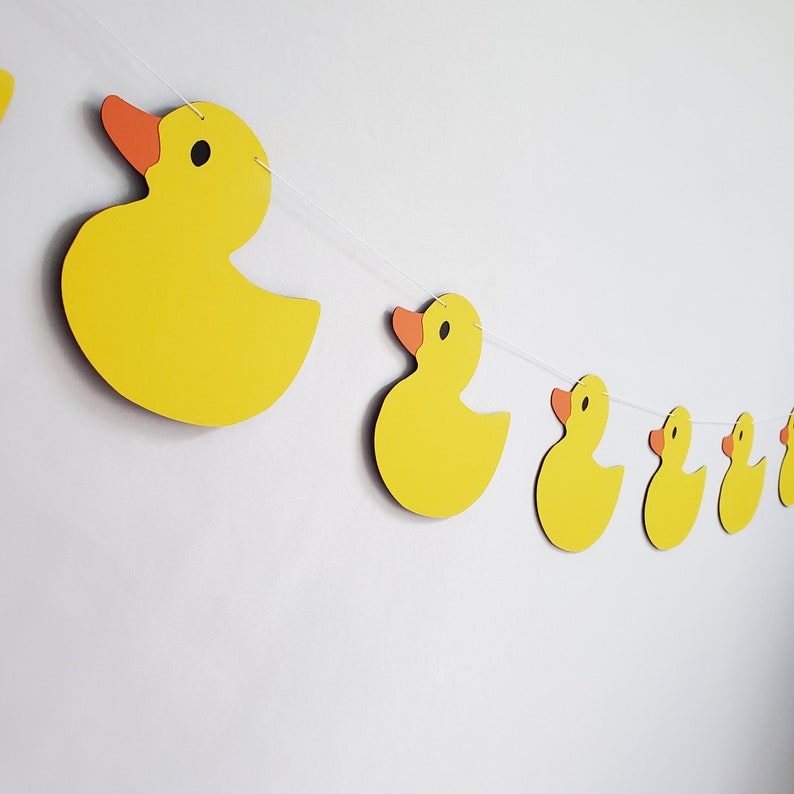 May include: A yellow rubber ducky garland with orange beaks and eyes. The garland is strung together with white string.