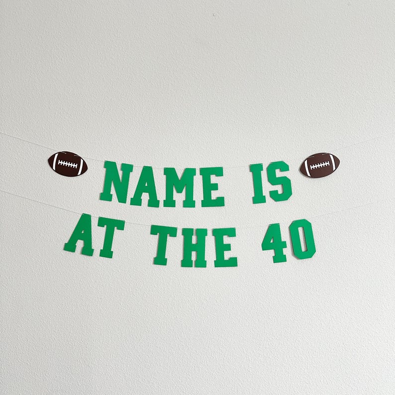 Puede incluir: Pancarta verde y blanca con el texto "NAME IS AT THE 40" y dos balones de f&uacute;tbol marrones en cada extremo.