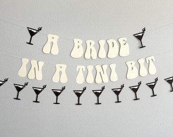 May include: A white banner with the text "A Bride in a Tini Bit" in a retro font. The banner is decorated with black martini glass cutouts.