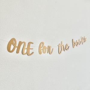 May include: A gold banner with the text "ONE for the books" hanging on a white wall.