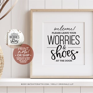 Puede incluir: Un cartel blanco con texto negro que dice "welcome! Please leave your worries & shoes at the door." El cartel está enmarcado en un marco de madera claro y está sentado en un estante blanco.