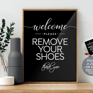 Op de afbeelding: Zwart-witte bord met de tekst "Welkom Alstublieft Schoenen uittrekken Dank u". Het bord is ingelijst in een houten lijst en staat op een houten oppervlak.