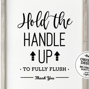 May include: A framed white sign with black text that reads "Hold the HANDLE UP to FULLY FLUSH. Thank You." The sign also includes a circular design that says "truly ORIGINAL DESIGNS BE CREATIVE DON'T COPY".